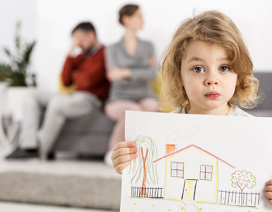 child holding drawing of home with parents fighting in background
